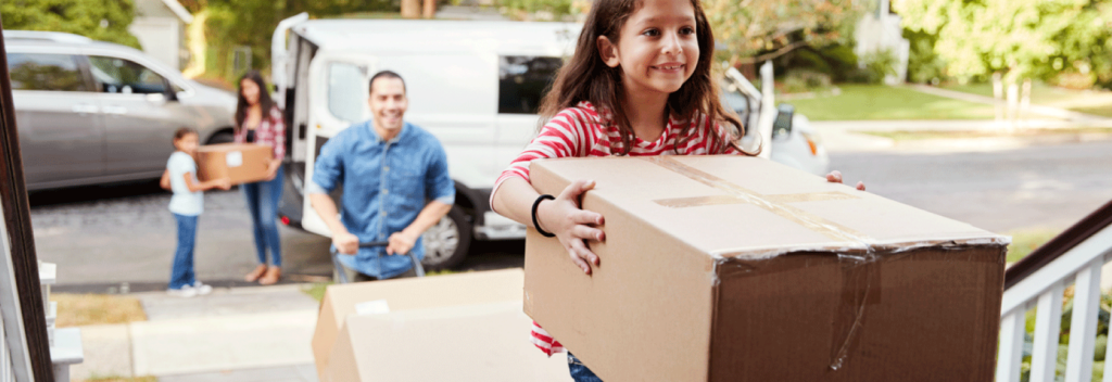 Little girl carrying box up flight of stairs with family trailing behind