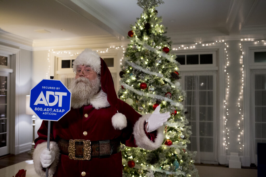 Santa holding an ADT sign with a Christmas tree behind