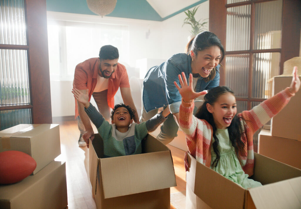 Military family laughing and playing with children in moving boxes during a home relocation.