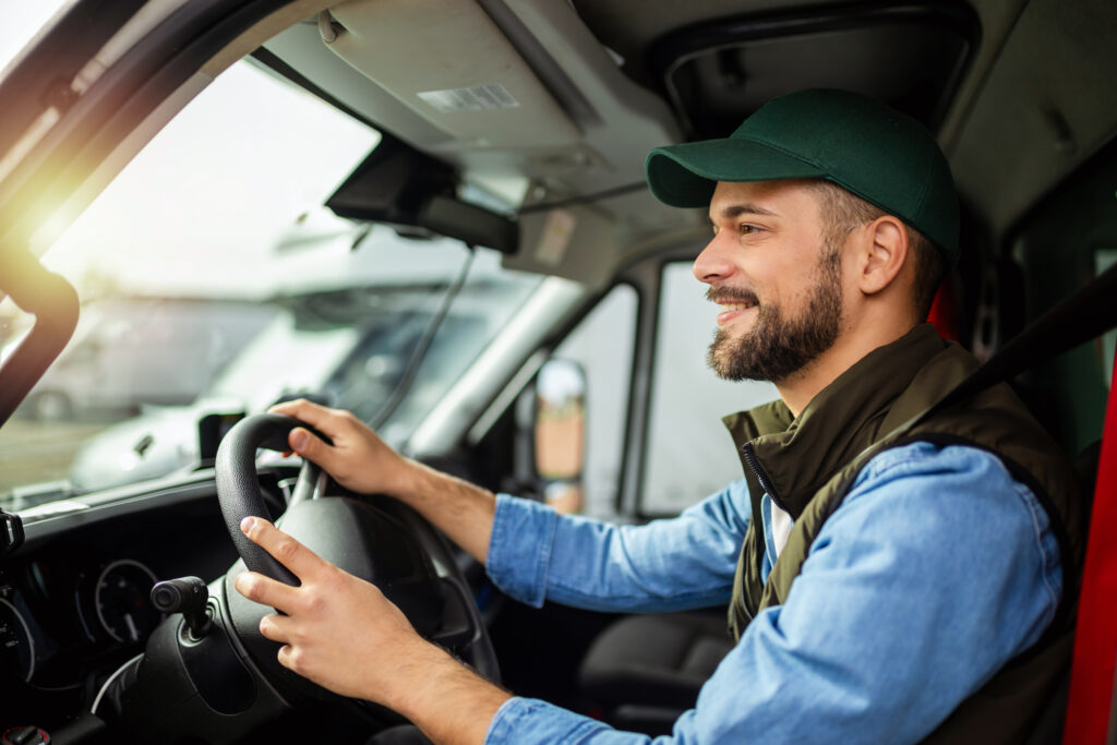 A bearded servicemember in a cap happily driving a moving truck during a military PCS, qualifying for non-locality BAH.